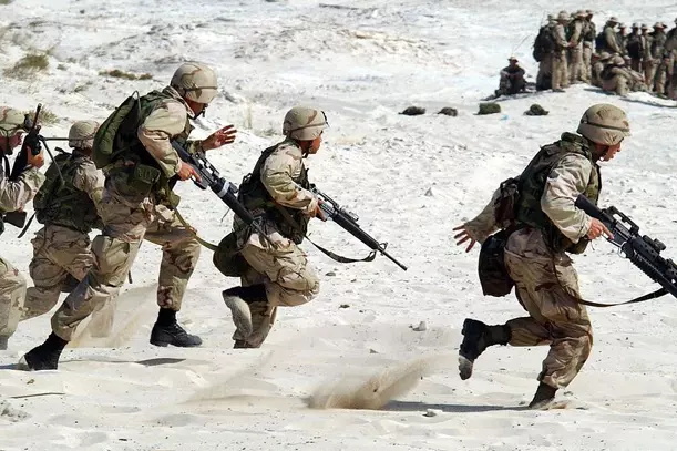 A bunch of military personals training and running in the sand.